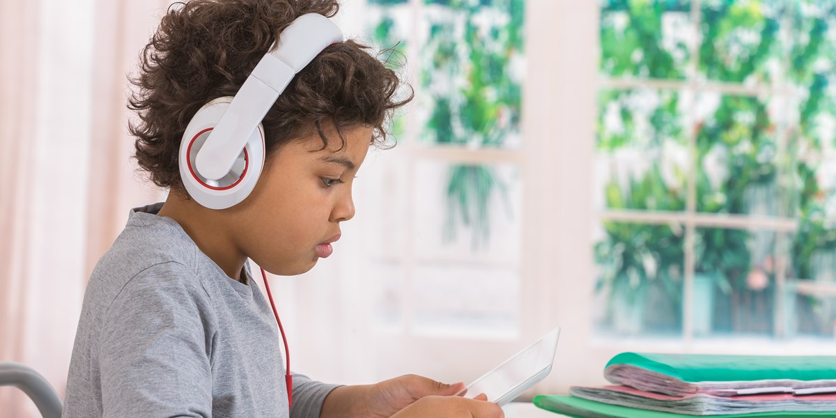 A child reads from a tablet computer while wearing headphones.